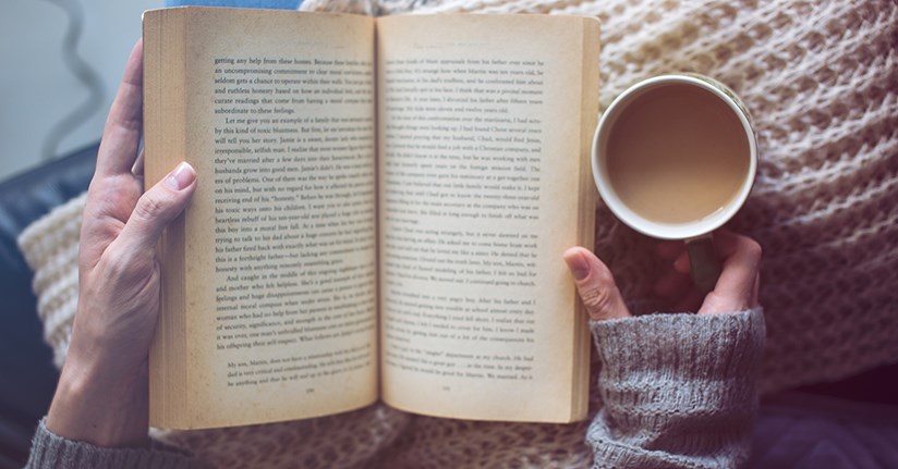 Person som läser en bok och dricker kaffe.