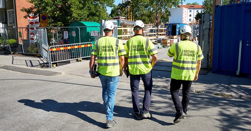Tre män klädda i gula västar med texten Rättvist byggande går mot en byggarbetsplats